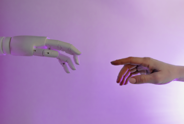 Two hands reach toward each other. One hand is human, the other is a robot hand.