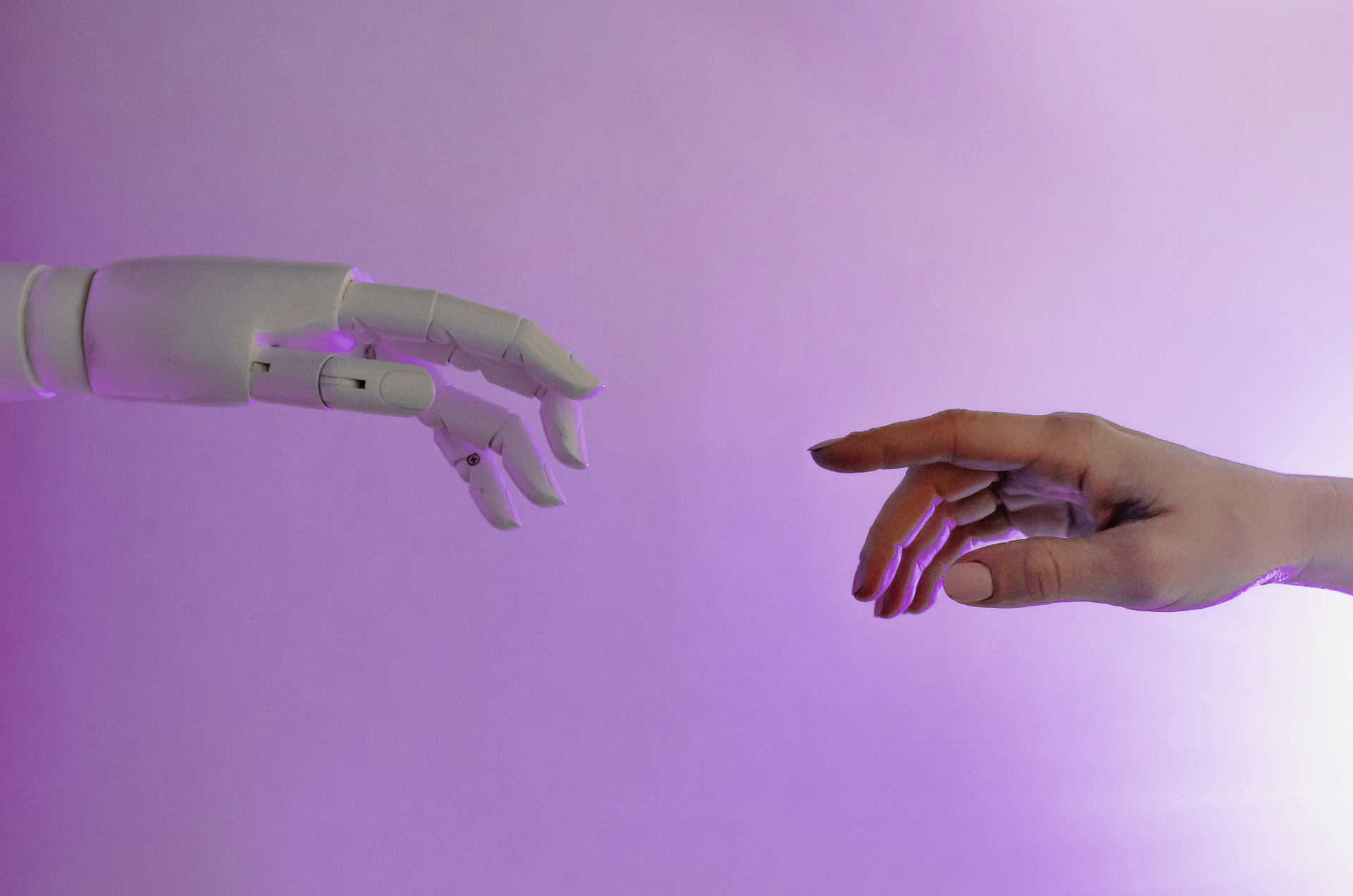 Two hands reach toward each other. One hand is human, the other is a robot hand.