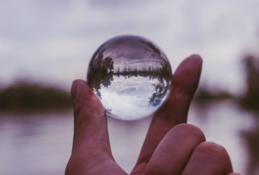Close up of a hand holding a glass orb with upside down lake and trees shown in the orb.