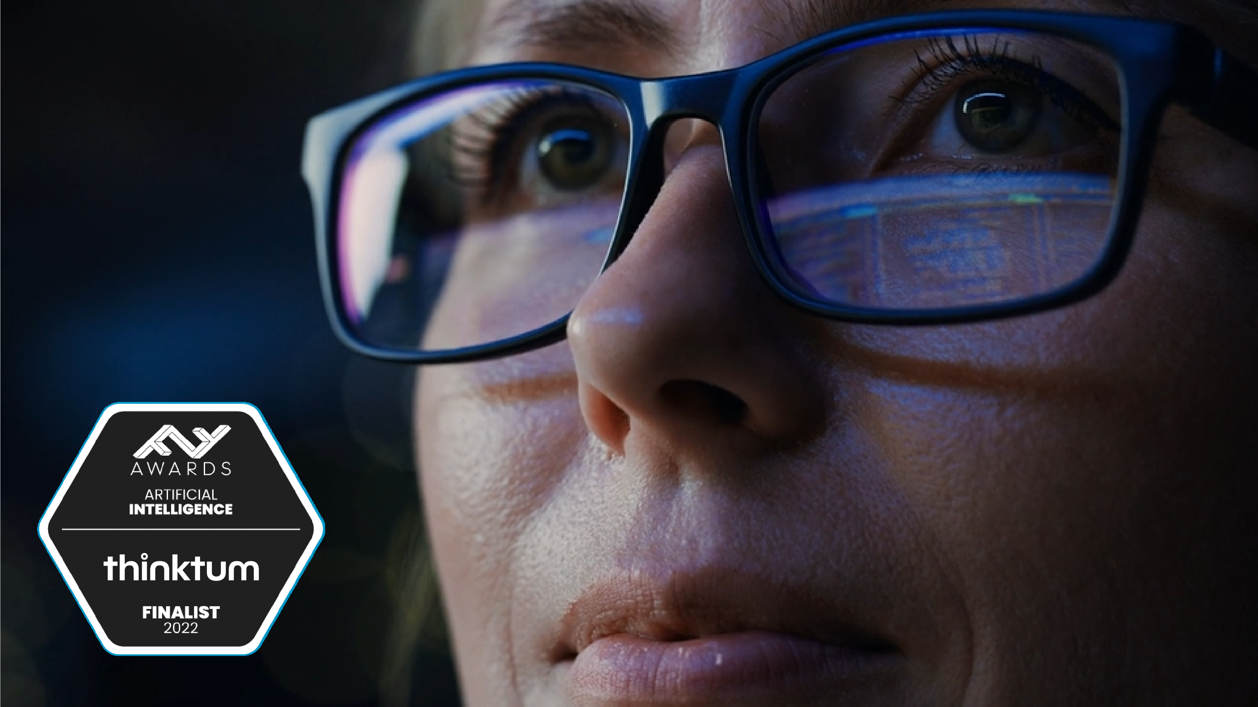 A close up of a person wearing glasses and looking away with a six-sided badge that reads: FF Awards Artificial Intelligence and thinktum with finalist 2022.