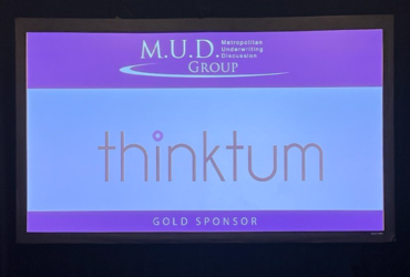 A monitor displays the Metropolitan Underwriting Discussion Group's wordmark as well as thinktum's and the words Gold Sponsor.
